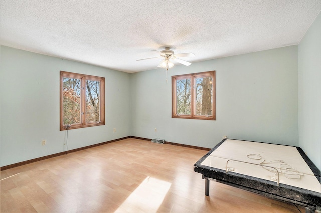 rec room with ceiling fan, light hardwood / wood-style floors, and a textured ceiling