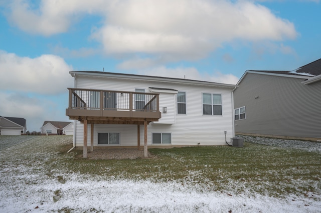 snow covered house with a wooden deck, cooling unit, and a lawn