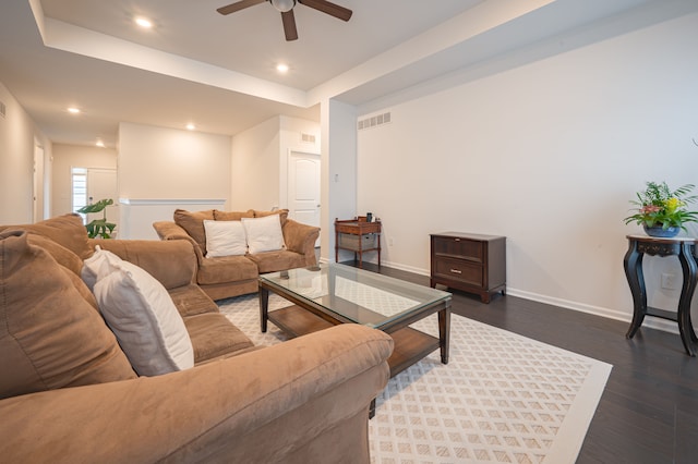 living room featuring a raised ceiling, ceiling fan, and dark wood-type flooring