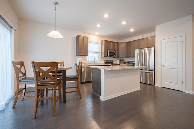 kitchen with light stone countertops, stainless steel appliances, dark hardwood / wood-style floors, a kitchen island, and hanging light fixtures