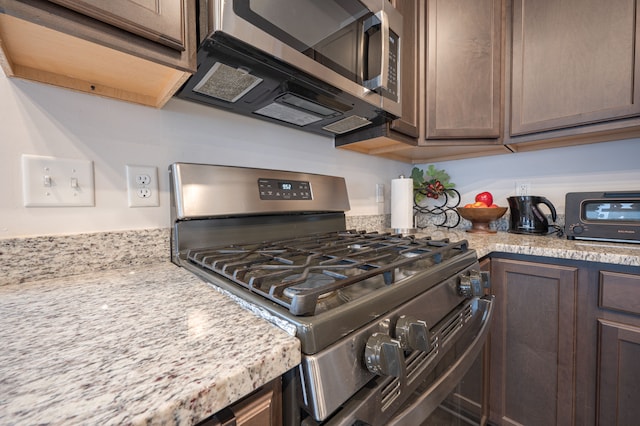 kitchen with dark brown cabinetry, light stone countertops, and appliances with stainless steel finishes