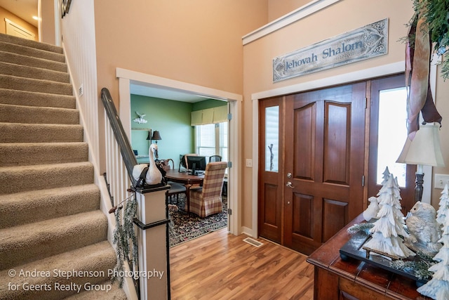 foyer entrance with a high ceiling, stairway, wood finished floors, and visible vents