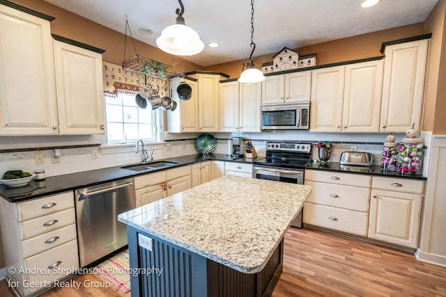 kitchen featuring dark stone countertops, a center island, decorative light fixtures, stainless steel appliances, and a sink