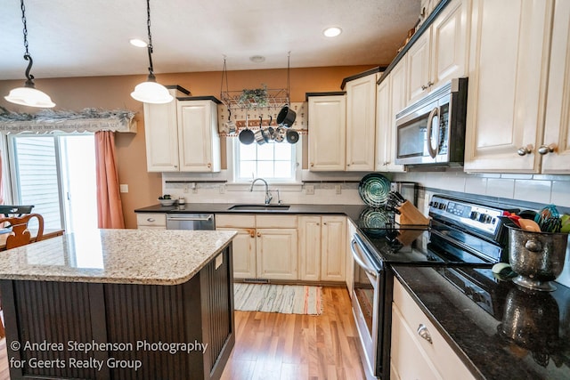 kitchen featuring appliances with stainless steel finishes, a center island, decorative light fixtures, and a sink