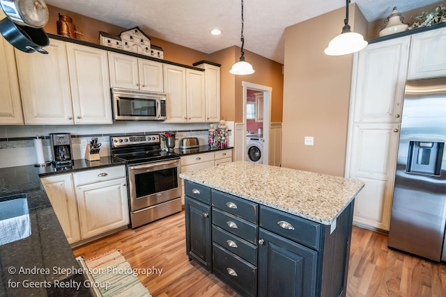 kitchen featuring hanging light fixtures, washer / dryer, a kitchen island, and appliances with stainless steel finishes