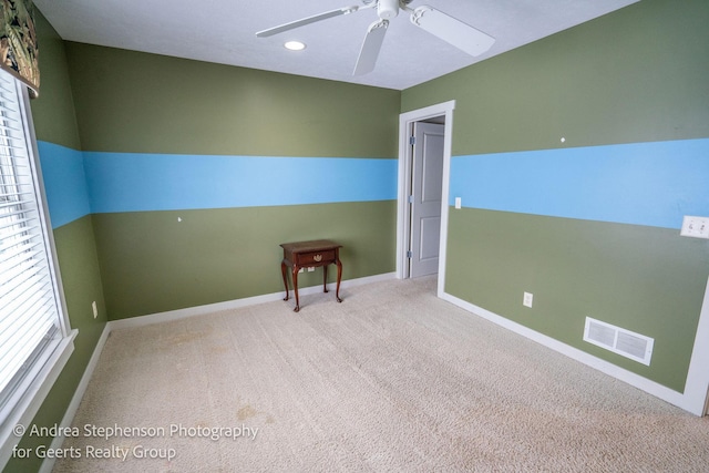 spare room with a ceiling fan, light colored carpet, visible vents, and baseboards