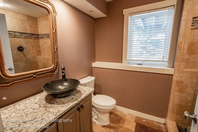 full bathroom with tiled shower, toilet, vanity, and baseboards