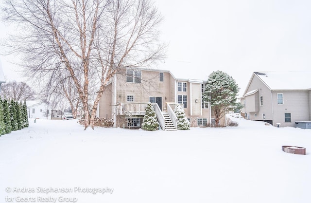 snow covered house with stairway and a wooden deck