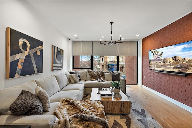living room with baseboards, a notable chandelier, light wood-style floors, and brick wall