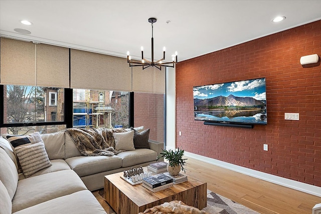 living room featuring baseboards, wood finished floors, a notable chandelier, and brick wall