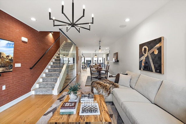 living area with stairs, a notable chandelier, light wood-style flooring, brick wall, and baseboards