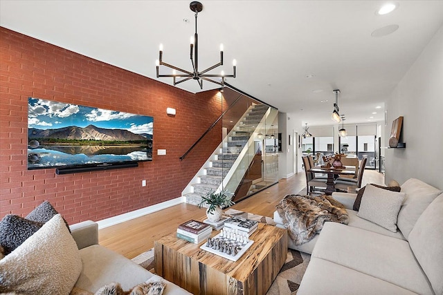 living room with a notable chandelier, stairway, light wood-style flooring, and brick wall