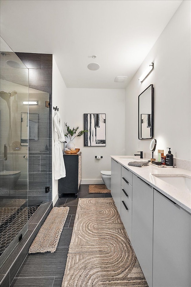 bathroom with a shower stall, baseboards, double vanity, toilet, and wood finish floors