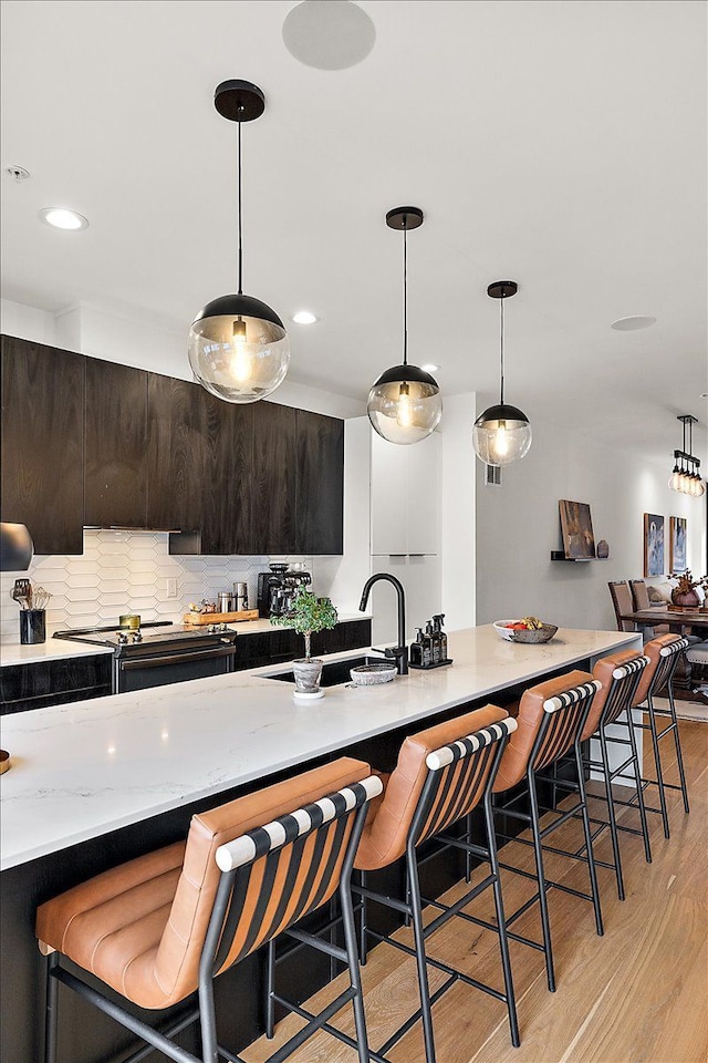 kitchen featuring a sink, backsplash, a breakfast bar area, range with electric stovetop, and light wood-style flooring