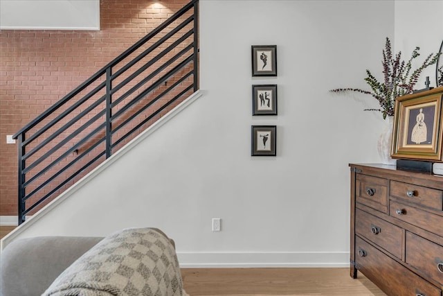 staircase with baseboards, wood finished floors, and brick wall
