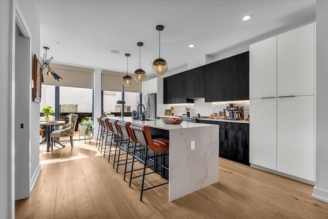 kitchen with a large island with sink, light wood finished floors, a kitchen bar, dark cabinetry, and modern cabinets