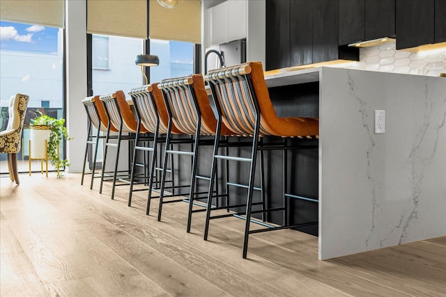 kitchen featuring a breakfast bar area, light wood-style floors, dark cabinets, and white cabinetry