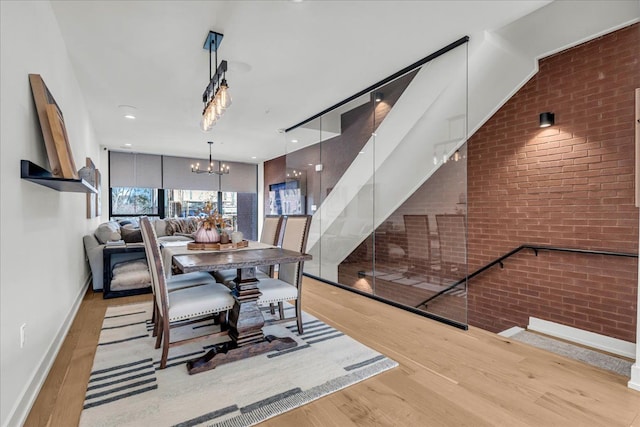 dining room featuring stairway, baseboards, brick wall, a notable chandelier, and wood finished floors