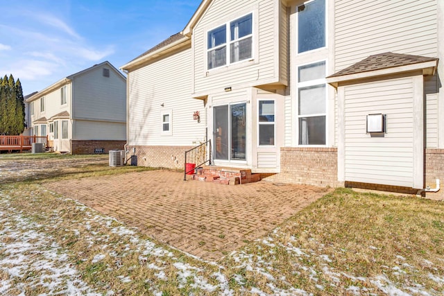 snow covered house with central AC unit and a patio