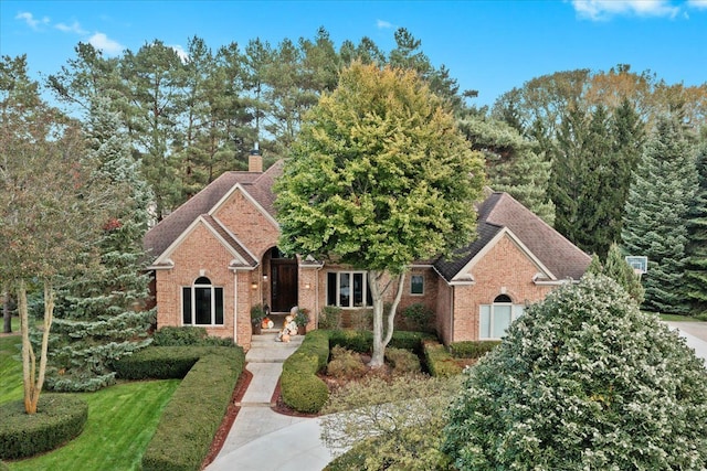 view of front of house with a shingled roof, a front yard, brick siding, and a chimney