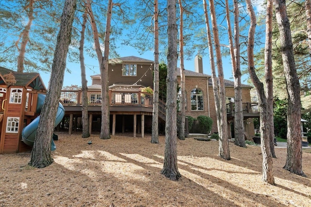 rear view of property with brick siding, a chimney, and a playground