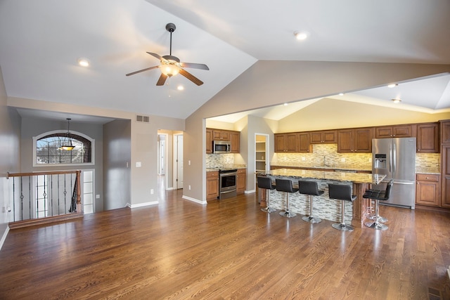 kitchen with dark hardwood / wood-style floors, tasteful backsplash, a kitchen bar, ceiling fan with notable chandelier, and appliances with stainless steel finishes