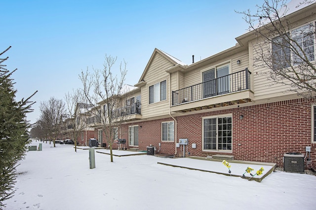 snow covered property with cooling unit and a balcony