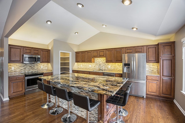 kitchen with dark stone countertops, stainless steel appliances, a center island, dark hardwood / wood-style floors, and lofted ceiling