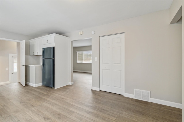 interior space featuring stainless steel fridge, light hardwood / wood-style flooring, and white cabinets