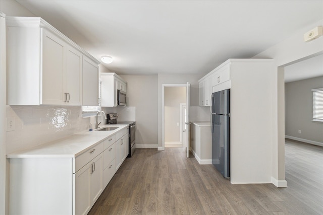 kitchen with backsplash, stainless steel appliances, sink, white cabinets, and light hardwood / wood-style floors