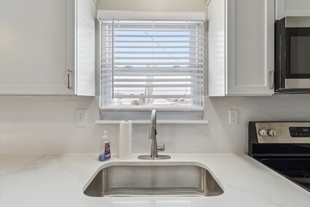 interior details featuring white cabinets, decorative backsplash, black range with electric stovetop, and sink