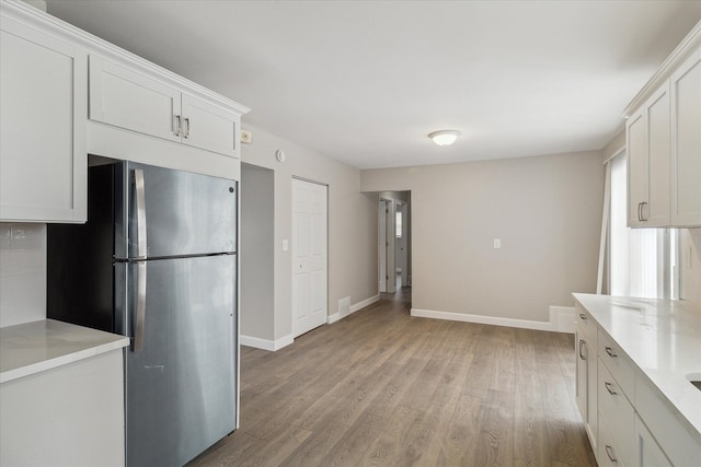 kitchen featuring white cabinetry, stainless steel fridge, light stone counters, and light wood-type flooring