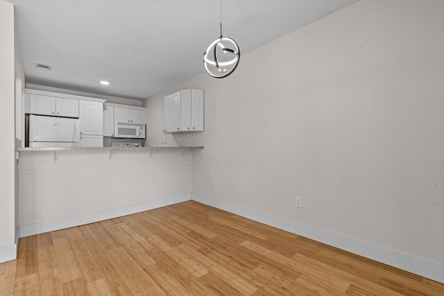 kitchen with white appliances, light stone counters, decorative light fixtures, light wood-type flooring, and white cabinets