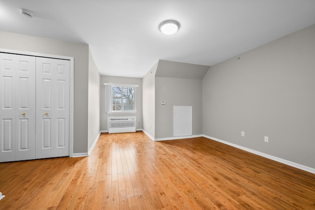 bonus room with vaulted ceiling, a wall mounted AC, and light hardwood / wood-style flooring