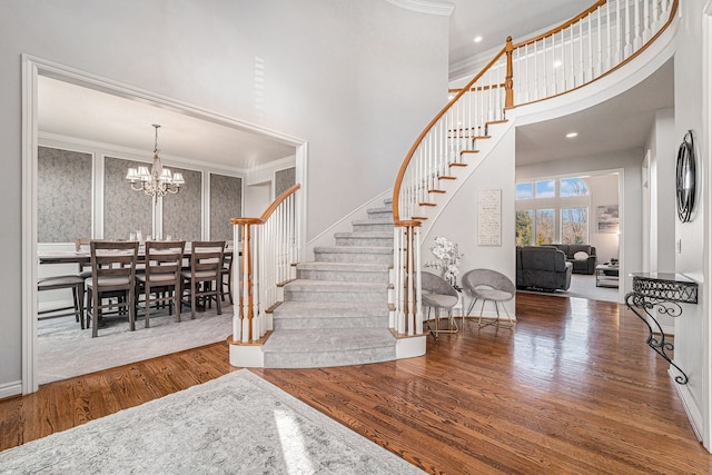 entrance foyer featuring a high ceiling, a notable chandelier, ornamental molding, and wood-type flooring