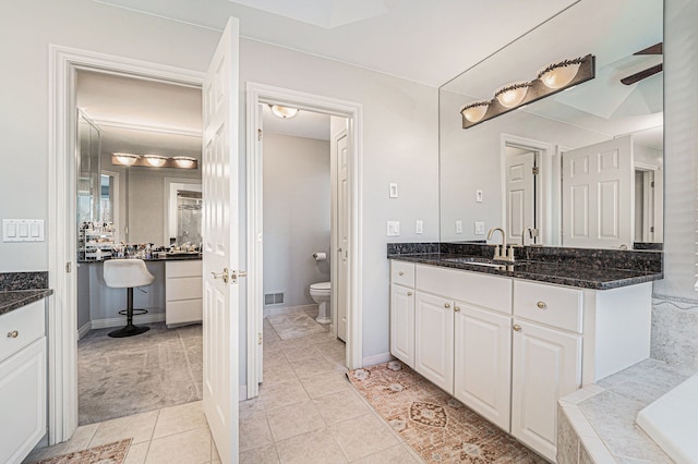 bathroom with vanity, tiled tub, tile patterned floors, and toilet