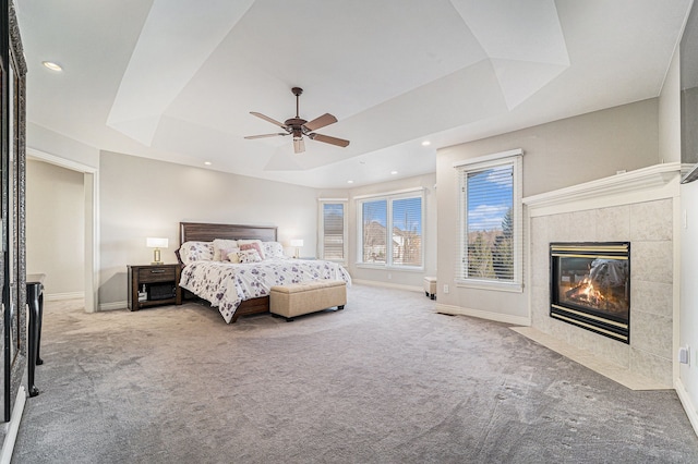 carpeted bedroom with ceiling fan, a raised ceiling, and a fireplace