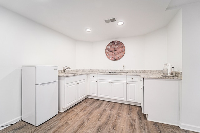 kitchen with white refrigerator, white cabinetry, light stone counters, light hardwood / wood-style floors, and black electric cooktop