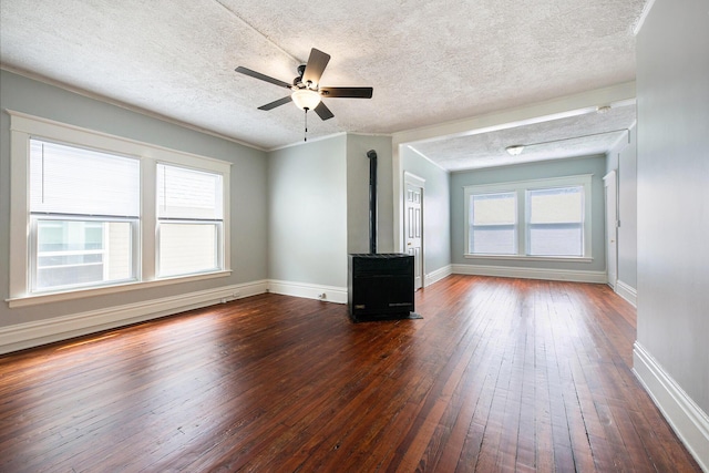 unfurnished living room with a wood stove, a wealth of natural light, dark hardwood / wood-style flooring, and ceiling fan