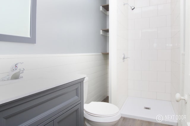 bathroom featuring tiled shower, vanity, toilet, and tile walls