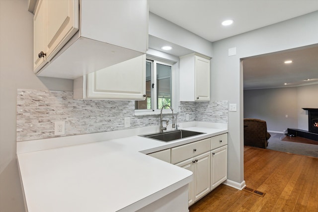 kitchen featuring decorative backsplash, sink, a wood stove, hardwood / wood-style floors, and white cabinetry