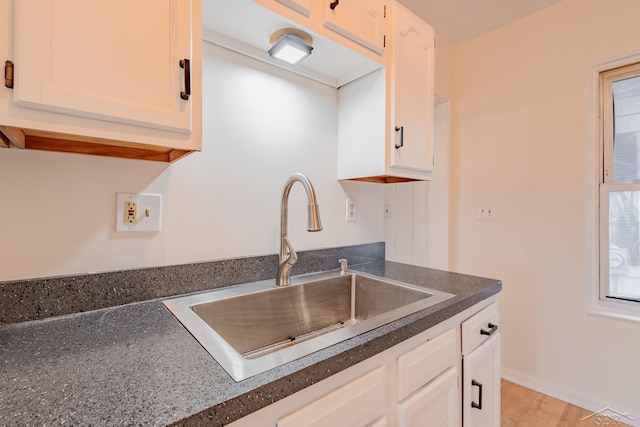 kitchen with light wood-type flooring, white cabinetry, and sink