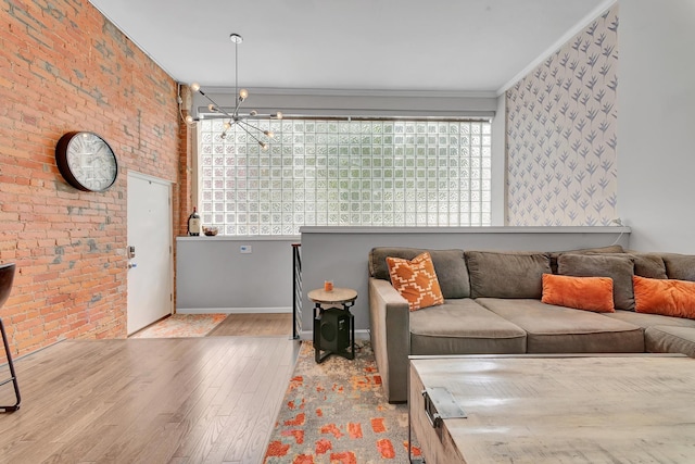 living room featuring brick wall, crown molding, light wood-type flooring, and a notable chandelier