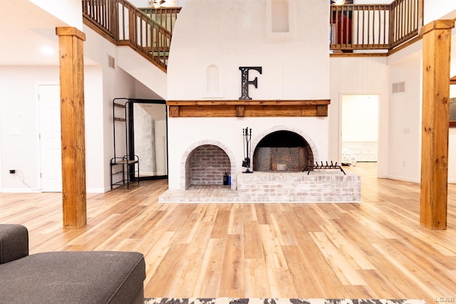 living room featuring wood-type flooring, a fireplace, a high ceiling, and decorative columns