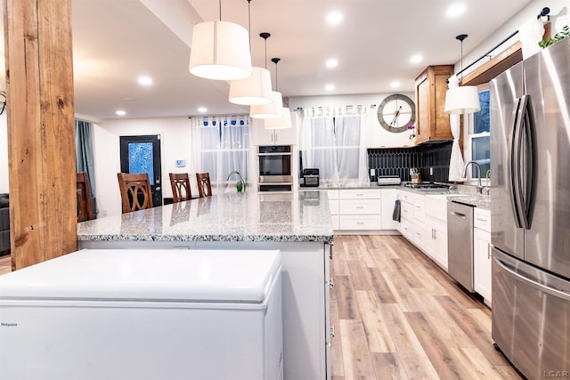 kitchen featuring appliances with stainless steel finishes, light stone counters, white cabinetry, hanging light fixtures, and a large island