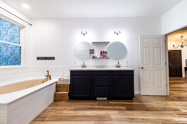 bathroom with a notable chandelier, vanity, a bathtub, and wood-type flooring