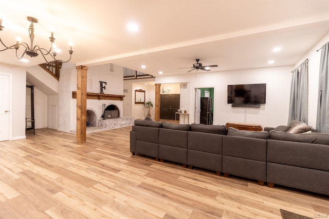 living room featuring ceiling fan with notable chandelier, light wood-type flooring, and a brick fireplace