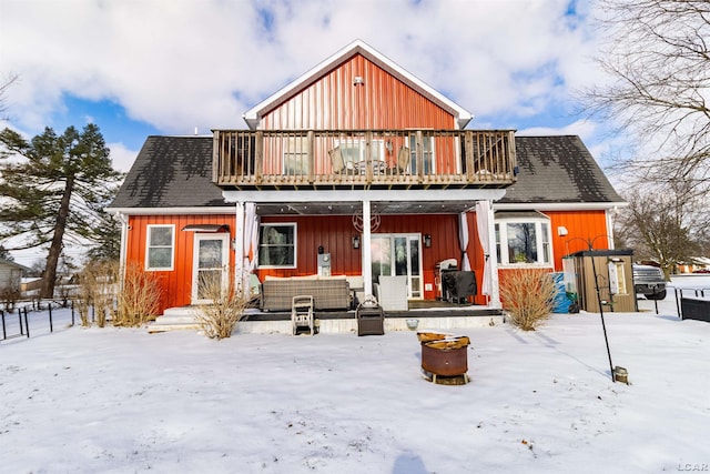 snow covered back of property with a balcony and an outdoor living space with a fire pit