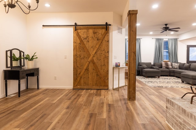 living room featuring a barn door, hardwood / wood-style floors, and ceiling fan with notable chandelier