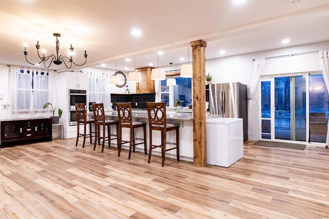 kitchen with pendant lighting, light wood-type flooring, stainless steel appliances, and a chandelier